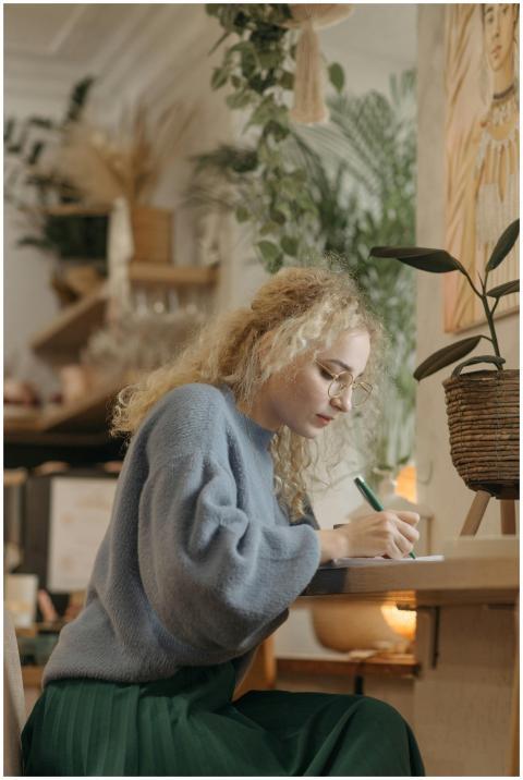 A young woman wearing a blue sweater writes at a t