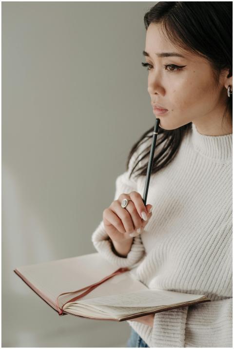 Thoughtful young woman holding a notebook and pen,