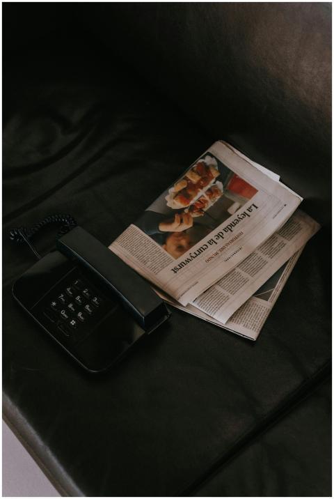 A vintage black telephone and newspaper on a dark