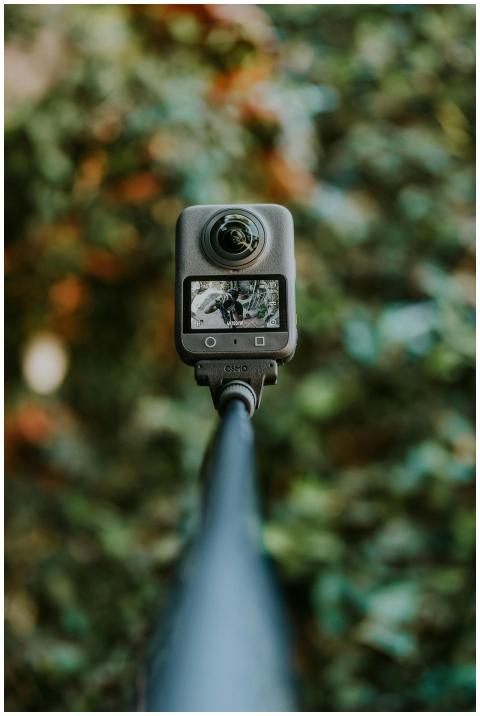 A 360 camera mounted on a pole with a blurred gree