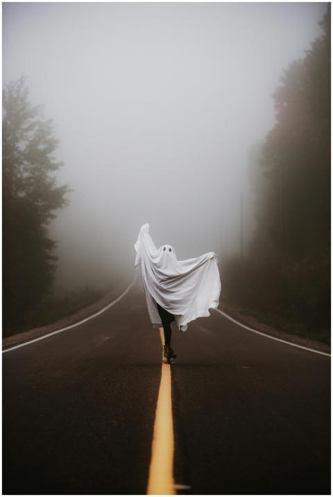 A person dressed as a ghost on a foggy road, embod