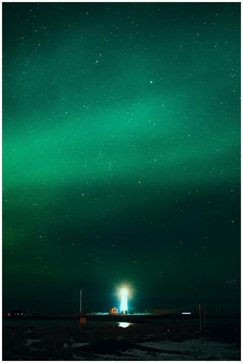 Beacon with glowing rays under colorful green sky