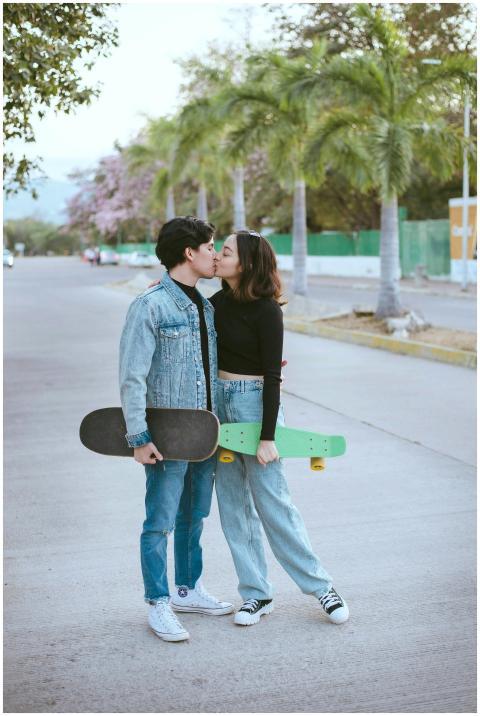 Teen couple sharing a kiss holding skateboards in
