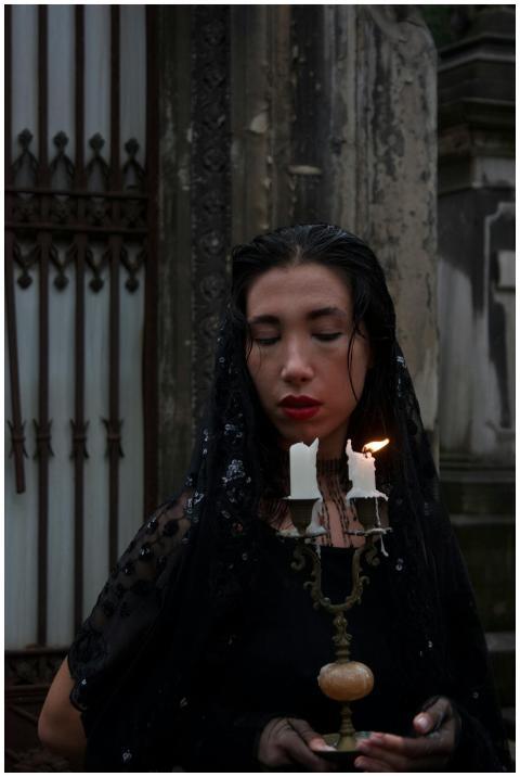 A woman with dark veil holding a lit candle in a g