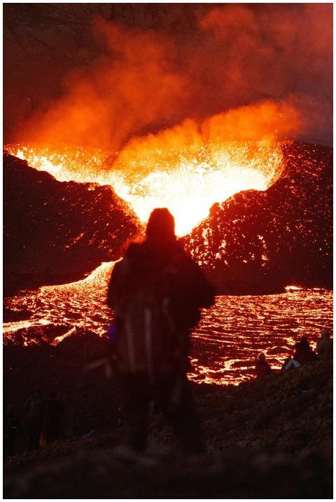 A person stands before a dramatic volcanic eruptio