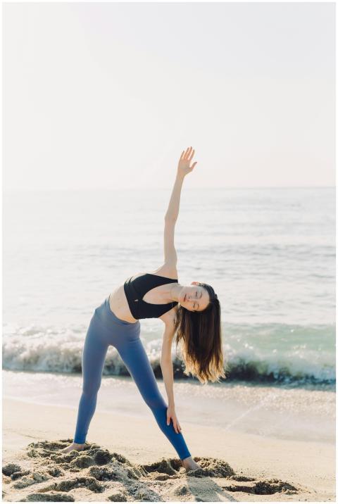 A woman stretches on a serene beach, embracing a h
