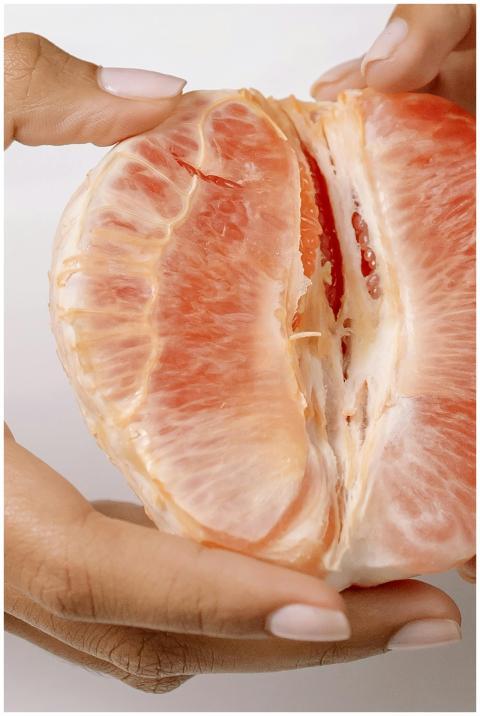 Detailed image of hands peeling a ripe grapefruit,