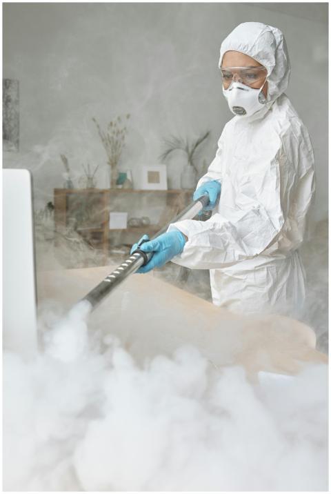 A woman in full protective gear disinfects a room