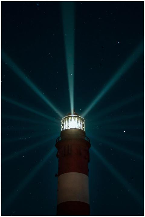 A lighthouse casts beams of light into the starry