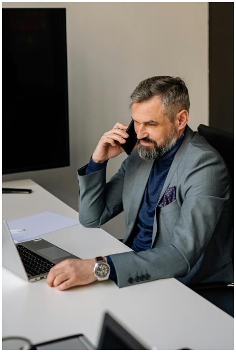 Bearded businessman in office using laptop and pho