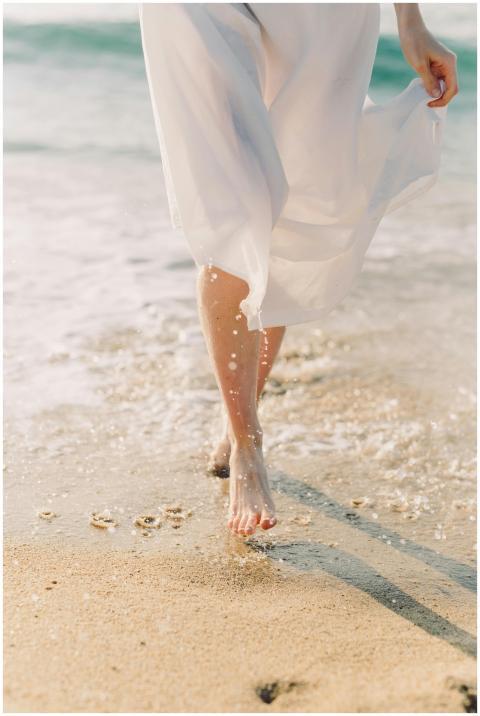 A woman in a white dress walks barefoot along a su