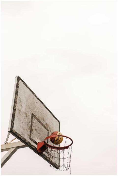 A basketball on the rim of a worn outdoor basketba