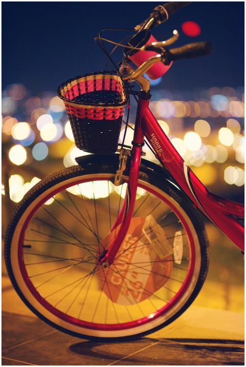 Red bicycle with a basket against blurred city lig