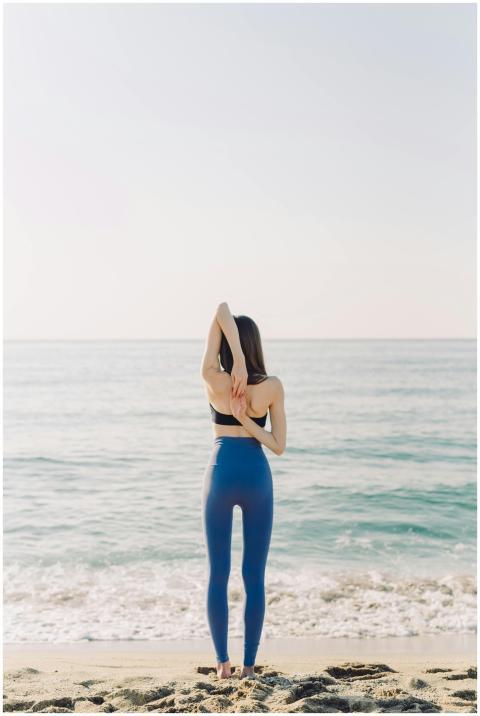 Rear view of a woman practicing yoga on a serene b
