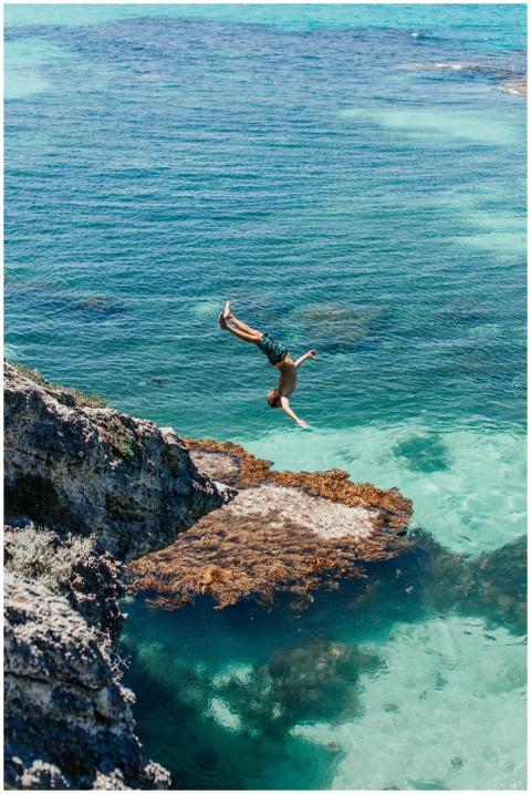 A man gracefully dives off a cliff into clear turq