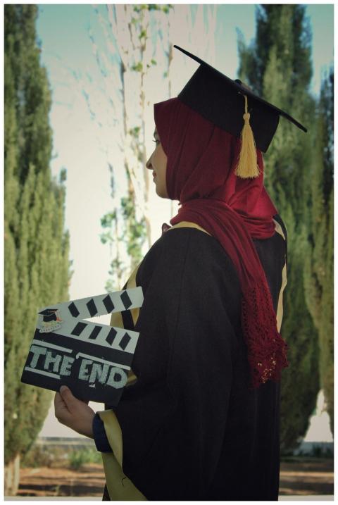Side view of Muslim graduate in hijab holding clap