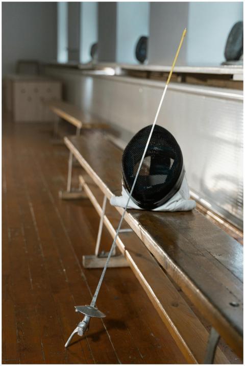A fencing mask and foil resting on a wooden bench