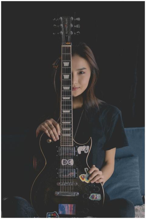 Asian woman sitting with an electric guitar, half-