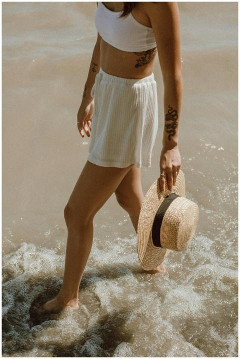 Woman with tattoos and straw hat walking on the be
