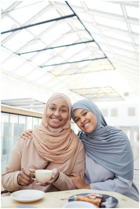 Two women in hijabs smiling and enjoying coffee in