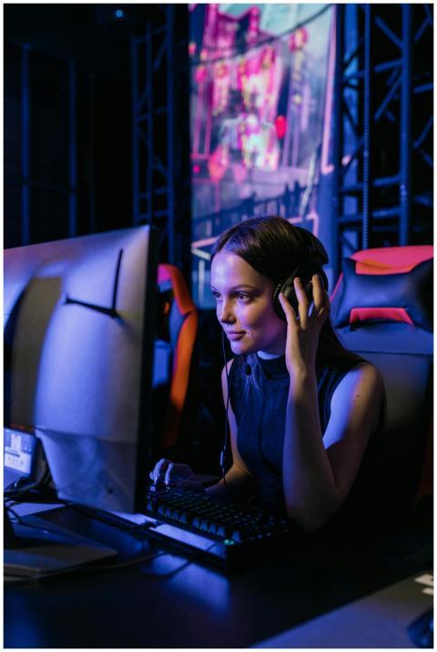 A woman gamer with a headset deeply focused on pla