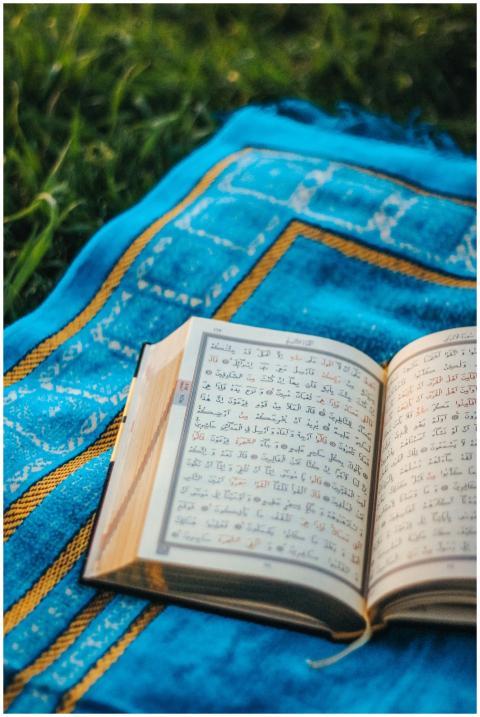 An open Quran rests on a blue prayer mat in an out