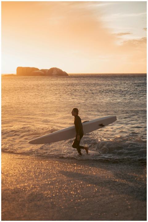 Man with surfboard walking on beach at sunset, gol