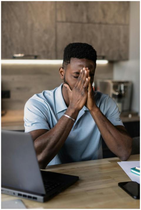 Man sitting at desk with laptop, showing frustrati