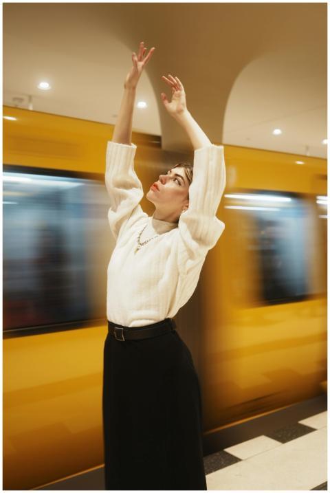 Young woman raises arms gracefully as a subway tra