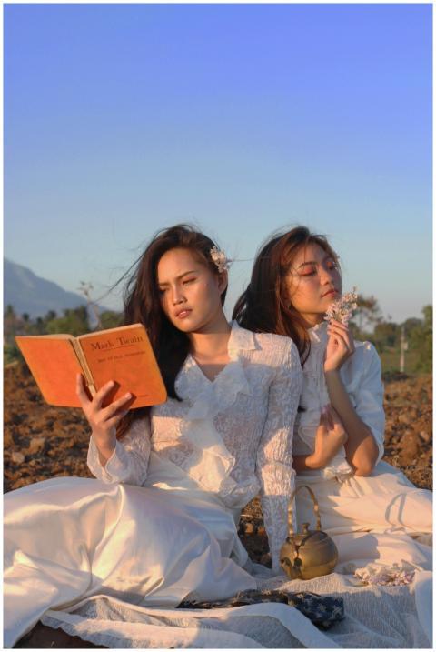Two women in white dresses reading outdoors at sun