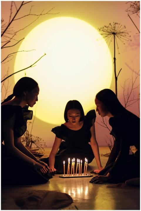 Three women in black dresses sit around glowing ca