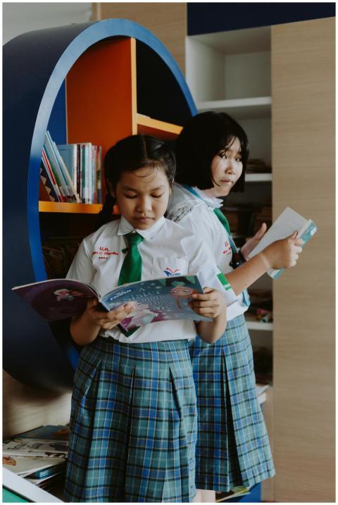 Two girls in school uniform reading books in a lib