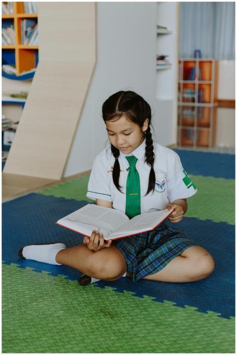 Girl in school uniform reading book on colorful fl