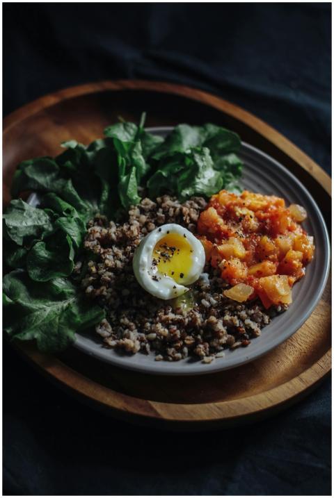 A rustic dish featuring greens, a poached egg, gro