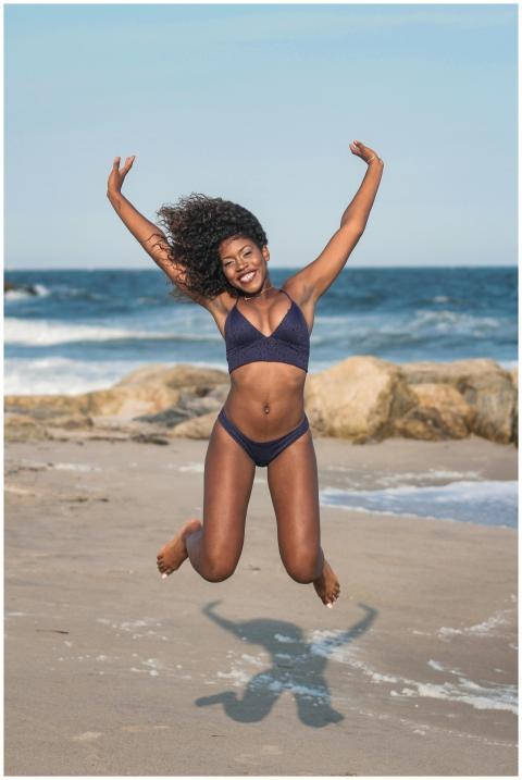 A woman in swimwear joyfully jumps on a sunny beac