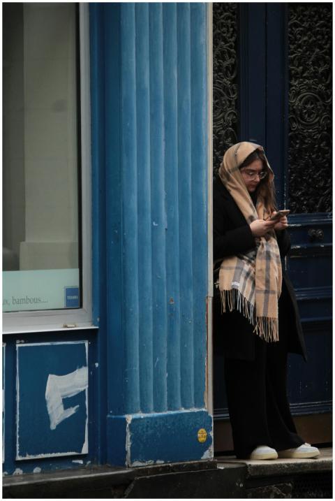 Woman in a scarf checking her phone by a blue stor