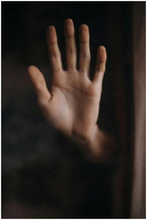 A close-up of an open human hand against a glass w
