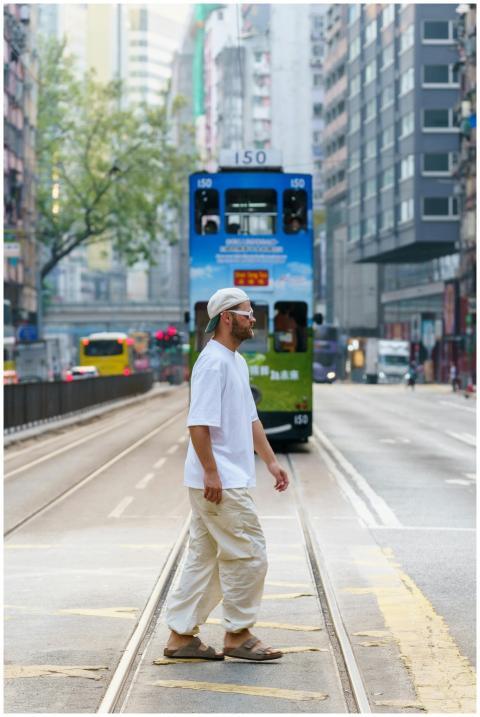 A man crossing a street in Hong Kong with a tram i