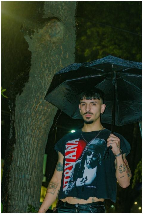 A stylish young man stands under an umbrella at ni