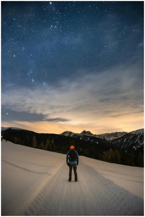A lone hiker gazes at the starry sky atop a snowy