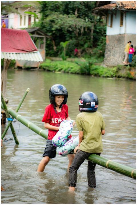 Two children wearing helmets play on a bamboo raft