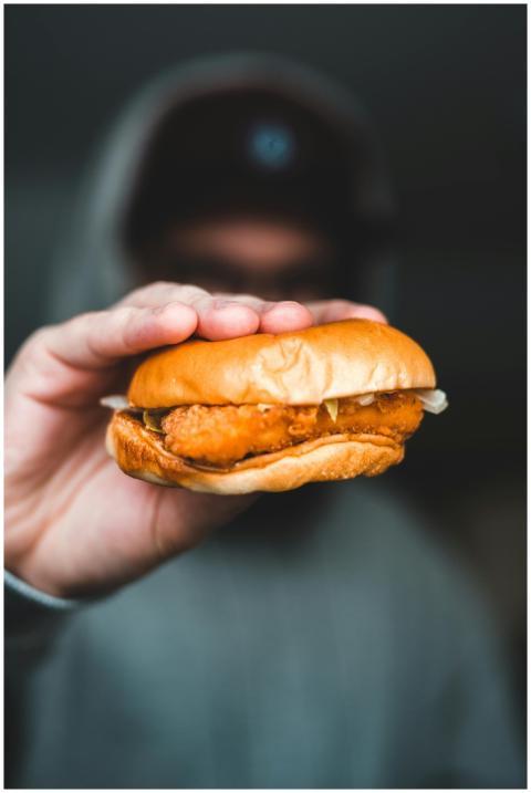 A hand holding a mouth-watering chicken burger, pe