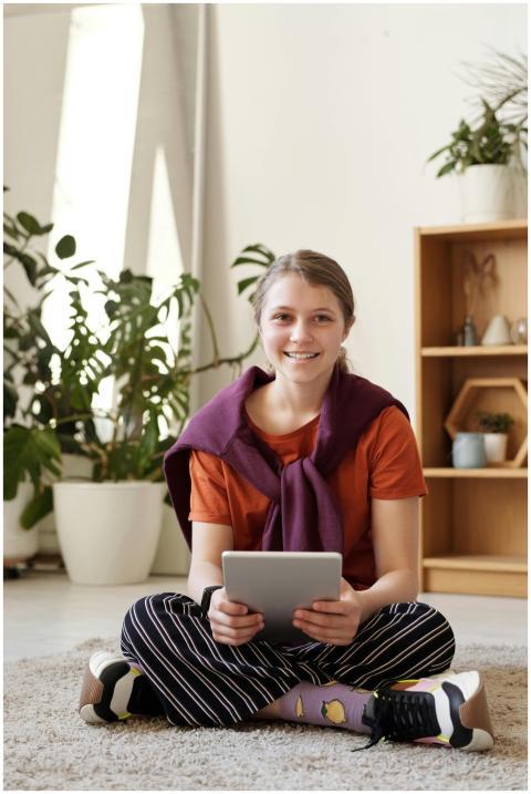Cheerful teenager sitting on the floor using a tab