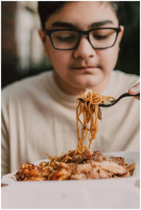 A teenage boy with glasses enjoys a takeout meal o