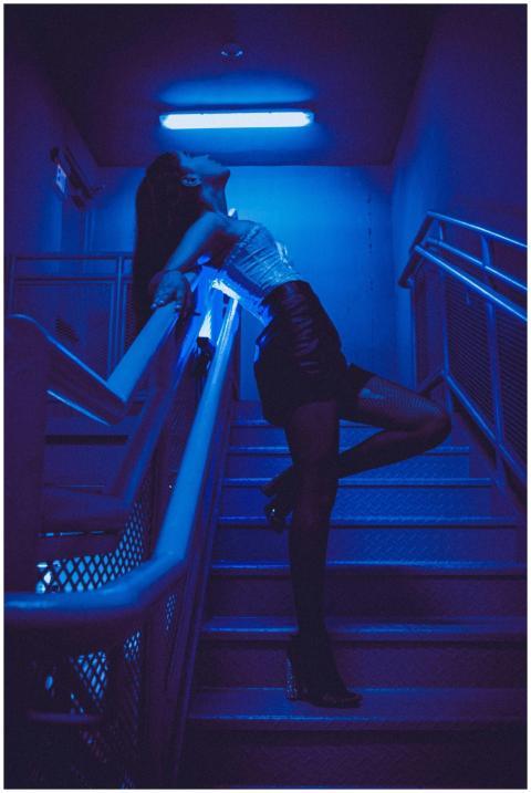 A woman strikes a dramatic pose on a neon-lit stai