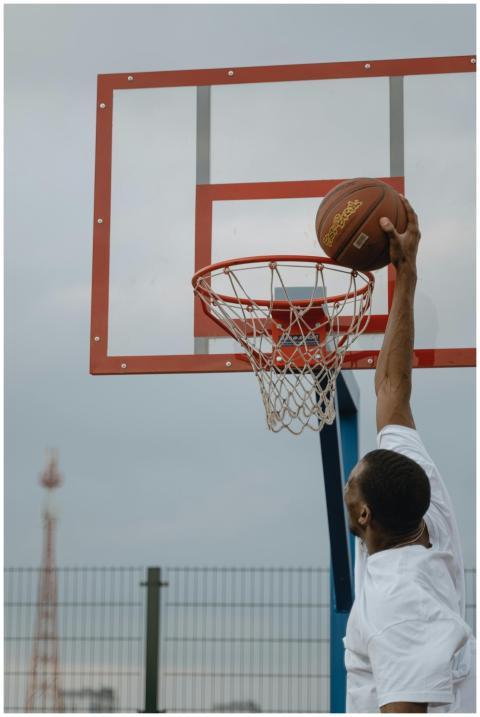 An energetic basketball player dunks on an outdoor