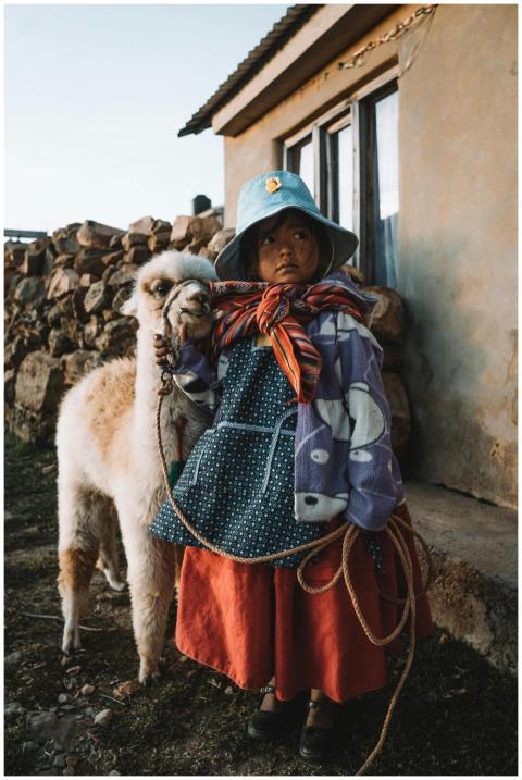 Young girl in traditional clothing with a llama, c