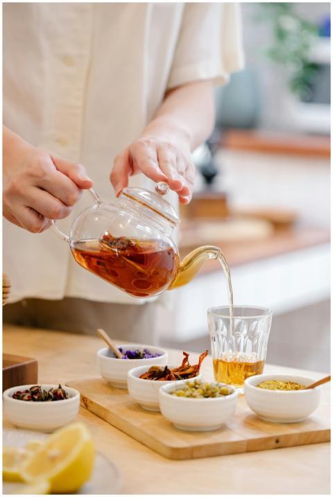 A person pouring herbal tea into a glass with vari