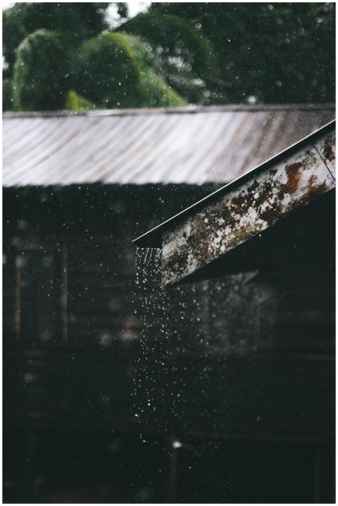 Glistening rain falls from a rusty metal roof, cre