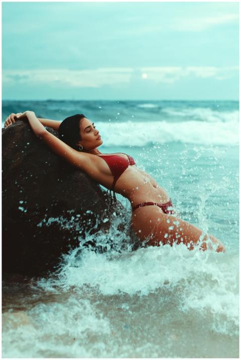 Elegant woman in a red bikini poses on a rock by t